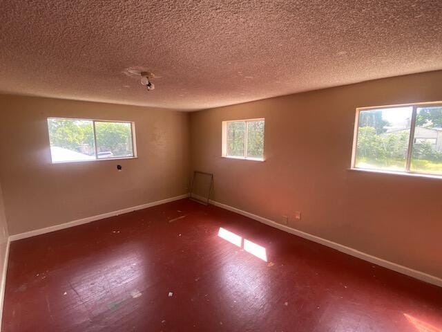 empty room featuring a textured ceiling, healthy amount of natural light, baseboards, and wood finished floors