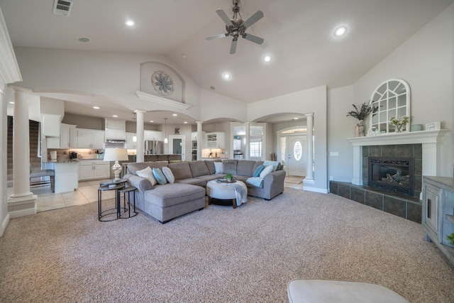 living room with ornate columns, light carpet, ceiling fan, a tile fireplace, and high vaulted ceiling