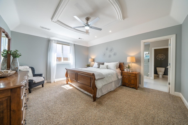 bedroom featuring light carpet, a tray ceiling, baseboards, and ensuite bath