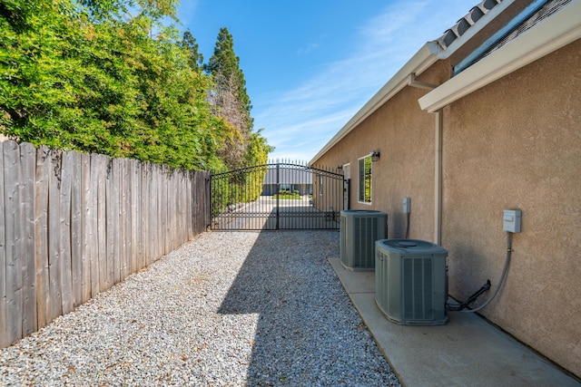 view of side of home featuring stucco siding, central AC, a gate, and fence