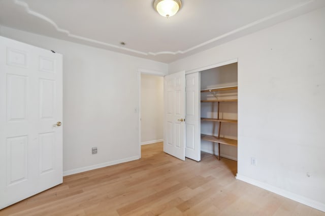 unfurnished bedroom featuring wood finished floors, baseboards, and a closet