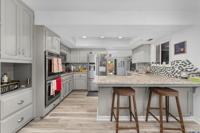7597 Terra Linda Way, Redding, CA 96003 - kitchen with appliances with stainless steel finishes, a peninsula, a tray ceiling, tasteful backsplash, and gray cabinets