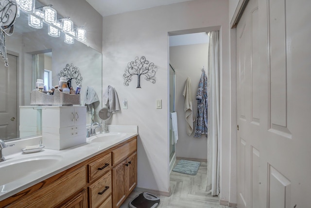 full bath featuring a stall shower, double vanity, and baseboards
