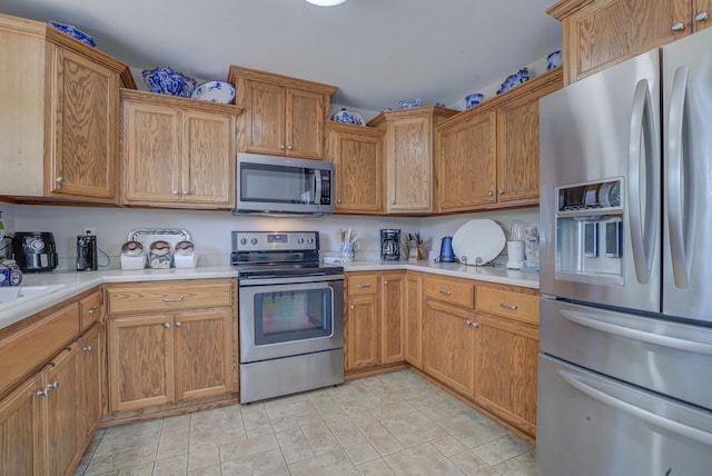kitchen with appliances with stainless steel finishes, light countertops, stone finish flooring, and brown cabinets
