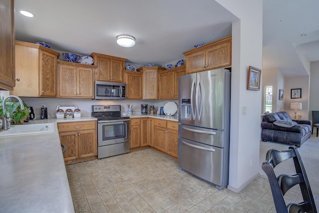 kitchen featuring appliances with stainless steel finishes, a sink, light countertops, light stone finish floors, and open floor plan