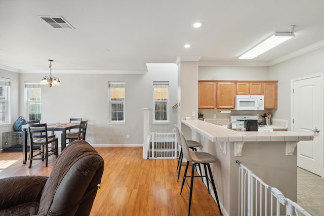 kitchen with white microwave, tile countertops, a breakfast bar area, range, and crown molding
