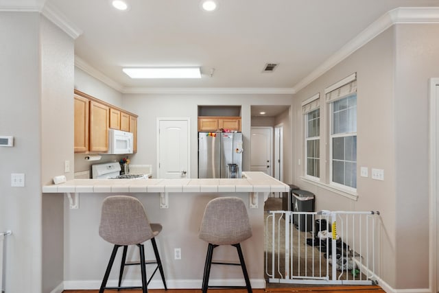 kitchen featuring white appliances, tile countertops, a peninsula, crown molding, and a breakfast bar area