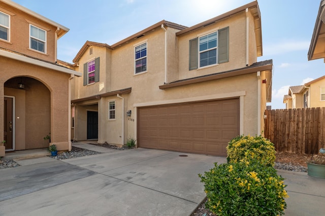 view of front facade with a garage, stucco siding, fence, and driveway