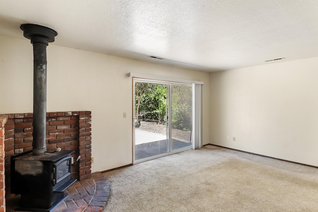 unfurnished living room with a wood stove, carpet flooring, baseboards, and a textured ceiling