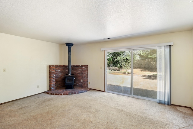 unfurnished living room featuring carpet, a wood stove, a textured ceiling, and baseboards