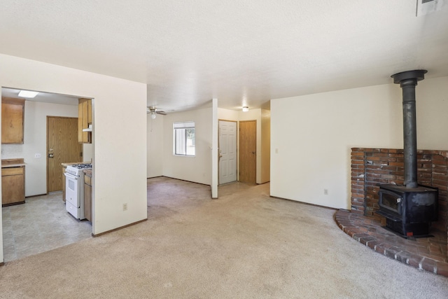 unfurnished living room with a wood stove, light colored carpet, ceiling fan, and baseboards
