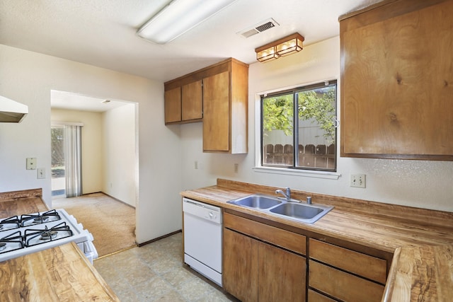 kitchen featuring white appliances, a sink, brown cabinetry, wood counters, and light carpet