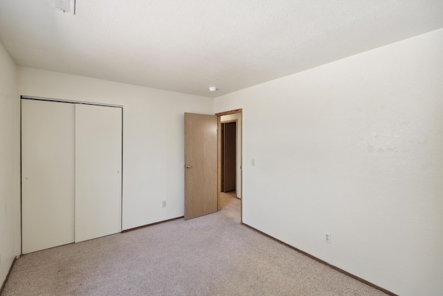 unfurnished bedroom with light carpet, a closet, and baseboards
