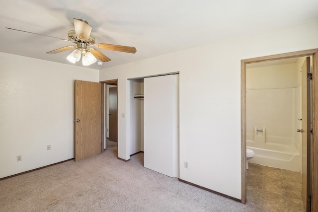 unfurnished bedroom with ensuite bath, a closet, baseboards, ceiling fan, and light carpet