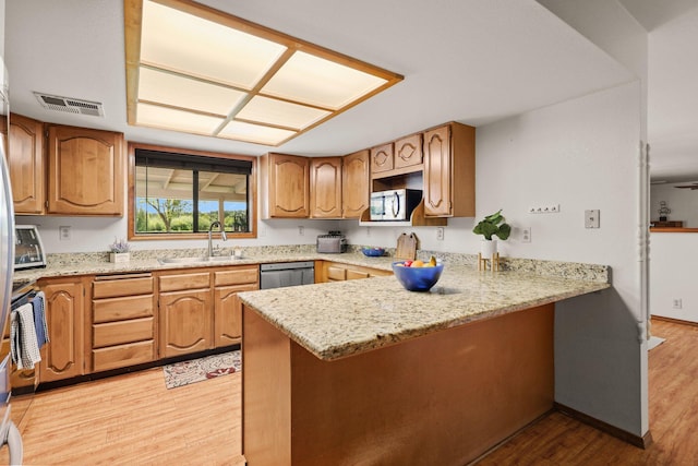 kitchen featuring stainless steel appliances, a sink, a peninsula, light wood-type flooring, and light stone countertops