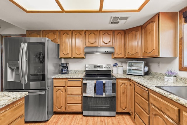 kitchen featuring stainless steel appliances, under cabinet range hood, light wood-style floors, brown cabinets, and a sink