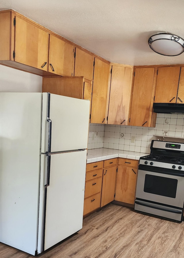 7670 Cedar Crest Rd, Shingletown, CA 96088 - kitchen featuring freestanding refrigerator, gas stove, under cabinet range hood, light wood finished floors, and tasteful backsplash