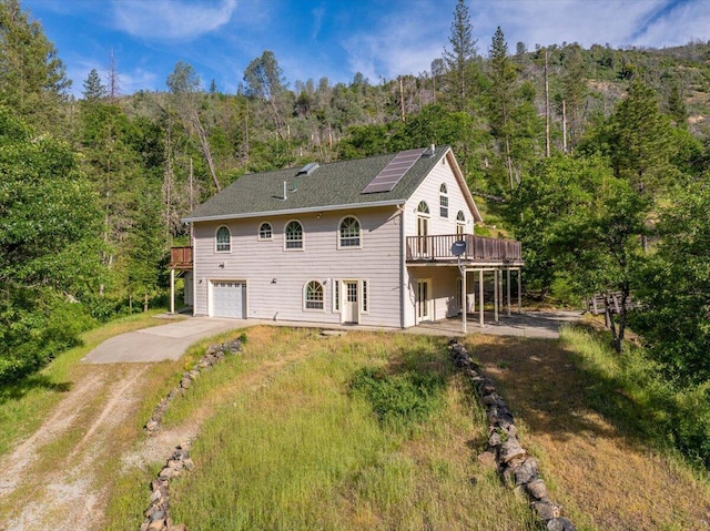 12876 E Fork Rd, French Gulch, CA 96033 - back of property with concrete driveway, an attached garage, a view of trees, a wooden deck, and roof mounted solar panels