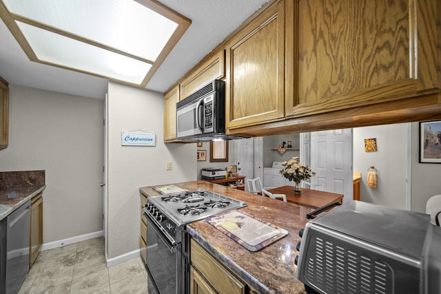 200 Ridgetop Dr # 26, Redding, CA 96003 - kitchen with appliances with stainless steel finishes, baseboards, washer / clothes dryer, dark stone counters, and brown cabinets