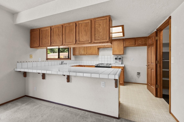 1152 Edgewood Dr, Redding, CA 96003 - kitchen with tile countertops, brown cabinets, stainless steel range with gas stovetop, and a peninsula