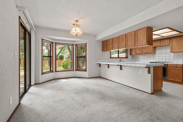 1152 Edgewood Dr, Redding, CA 96003 - kitchen with stainless steel range with gas stovetop, tile counters, light colored carpet, a breakfast bar area, and a textured ceiling