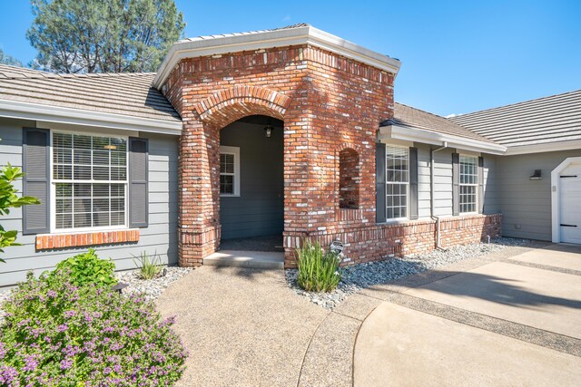 entrance to property with brick siding, an attached garage, and a tiled roof