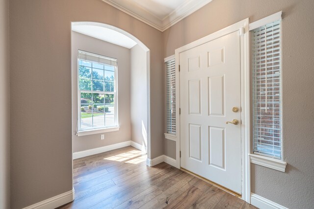 foyer with ornamental molding, wood-type flooring, arched walkways, and baseboards