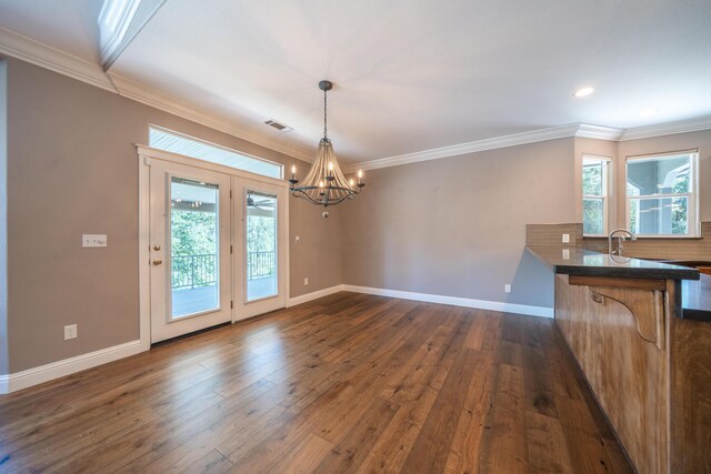 unfurnished dining area featuring a chandelier, dark wood-style floors, crown molding, baseboards, and a sink
