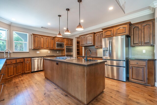 kitchen with appliances with stainless steel finishes, a sink, dark countertops, a kitchen island with sink, and crown molding