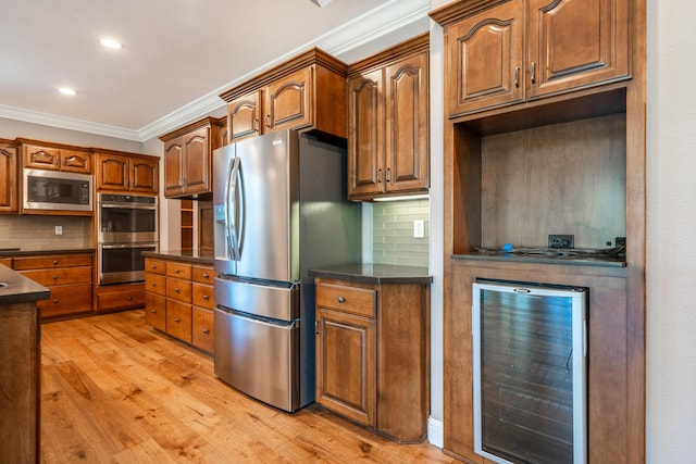 kitchen with appliances with stainless steel finishes, wine cooler, dark countertops, crown molding, and light wood-type flooring