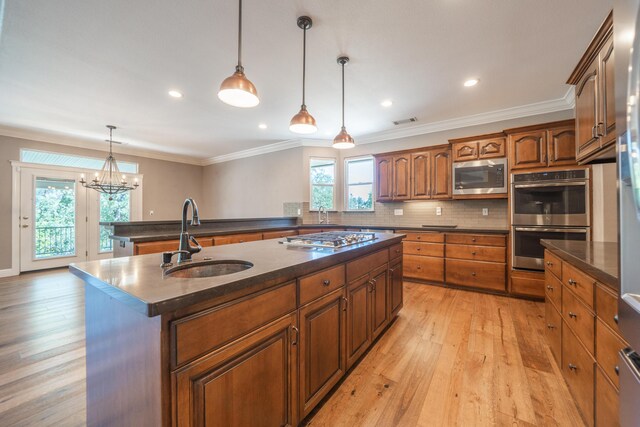 kitchen with stainless steel appliances, a sink, a kitchen island with sink, light wood finished floors, and backsplash