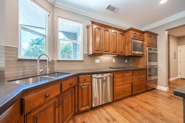 kitchen featuring appliances with stainless steel finishes, a sink, brown cabinets, light wood-type flooring, and tasteful backsplash