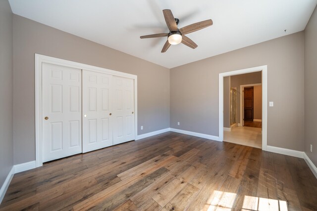 unfurnished bedroom with dark wood finished floors, a closet, baseboards, and ceiling fan