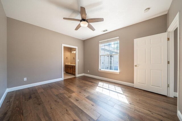 unfurnished bedroom featuring dark wood-style flooring, baseboards, ensuite bath, and ceiling fan