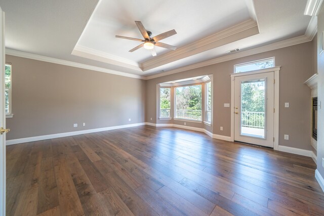 spare room featuring a raised ceiling, a ceiling fan, dark wood-type flooring, a glass covered fireplace, and crown molding