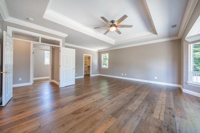 unfurnished bedroom with a raised ceiling, dark wood-style flooring, ornamental molding, baseboards, and a spacious closet
