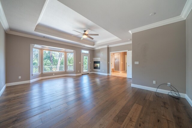 unfurnished living room featuring a ceiling fan, a tray ceiling, dark wood finished floors, baseboards, and crown molding