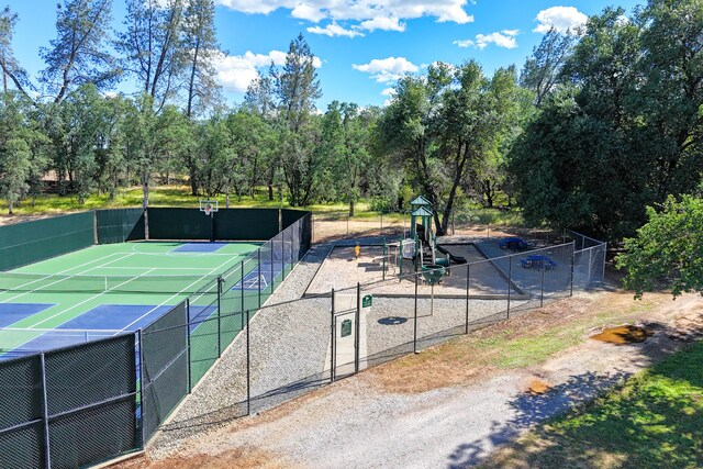 view of tennis court featuring fence, community basketball court, and view of wooded area