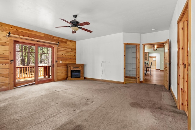 7185 Whispering Winds Ct, Shingletown, CA 96088 - unfurnished living room with carpet floors, wood walls, a glass covered fireplace, ceiling fan, and baseboards