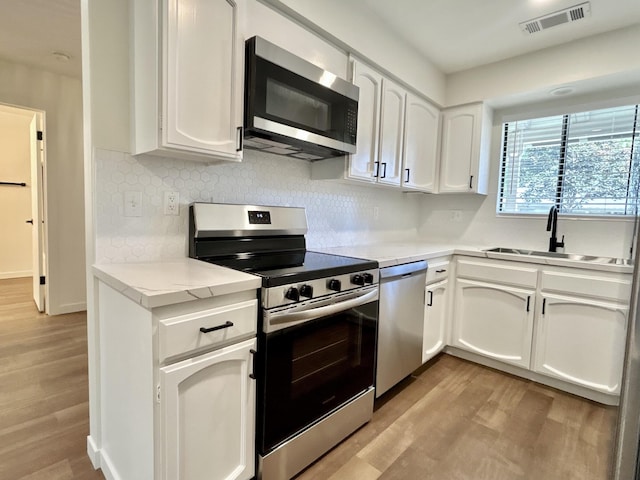1808 Del Mar Ave, Redding, CA 96003 - kitchen with stainless steel appliances, a sink, white cabinetry, light wood finished floors, and decorative backsplash