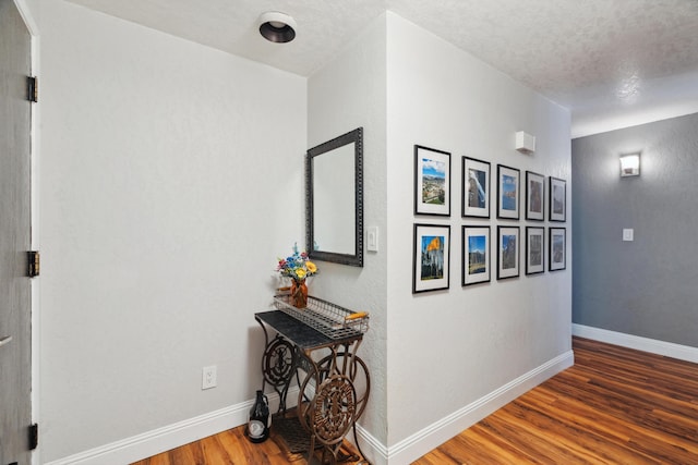 hall with wood finished floors, baseboards, and a textured ceiling