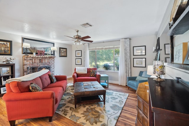 living room with ceiling fan, a brick fireplace, wood finished floors, and baseboards