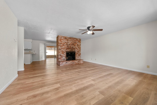 unfurnished living room featuring ceiling fan, light wood-style flooring, baseboards, and a brick fireplace