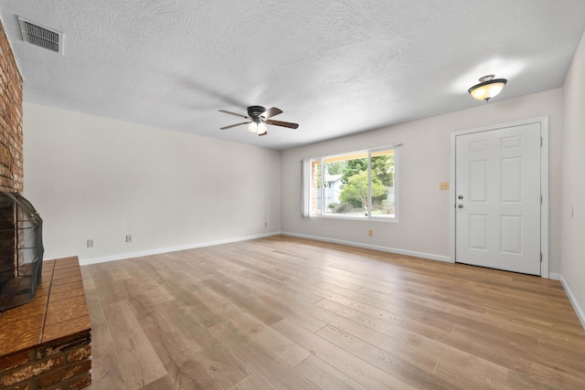 unfurnished living room with ceiling fan, light wood-type flooring, a wood stove, a textured ceiling, and baseboards