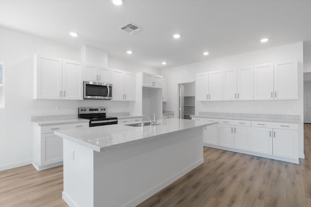 5555 Feathers Ave, Redding, CA 96002 - kitchen featuring appliances with stainless steel finishes, a sink, light wood finished floors, white cabinetry, and an island with sink