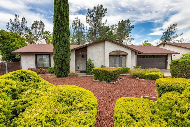 view of front facade with an attached garage, stucco siding, and fence