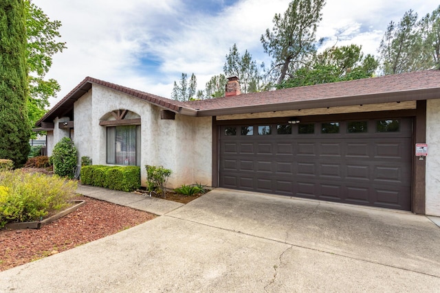 view of front of home with driveway, an attached garage, stucco siding, and a chimney