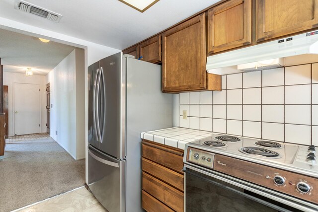 kitchen featuring range with electric cooktop, under cabinet range hood, freestanding refrigerator, tile countertops, and light colored carpet