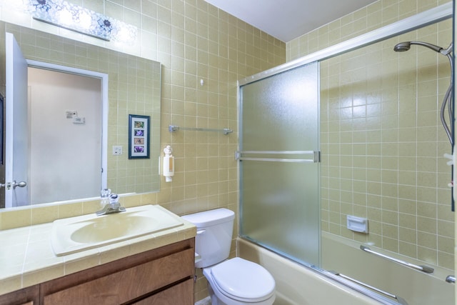 bathroom featuring vanity, bath / shower combo with glass door, tile walls, and toilet