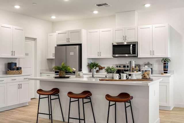 4148 Haleakala Ave, Redding, CA 96001 - kitchen with stainless steel appliances, a breakfast bar, light wood finished floors, a kitchen island with sink, and white cabinets